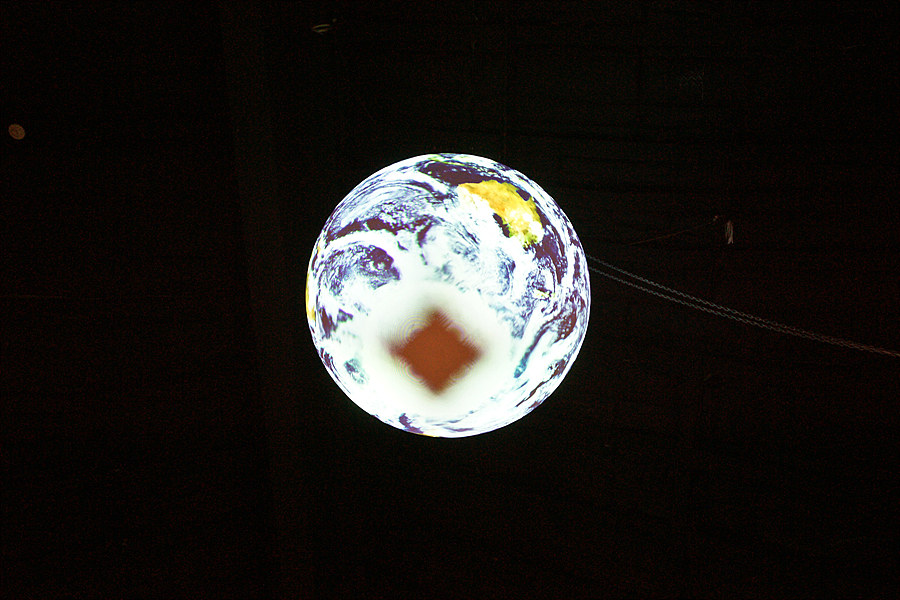 A dark brown diamond shape appears at the bottom of Science On a Sphere while it displays satellite imagery of Earth