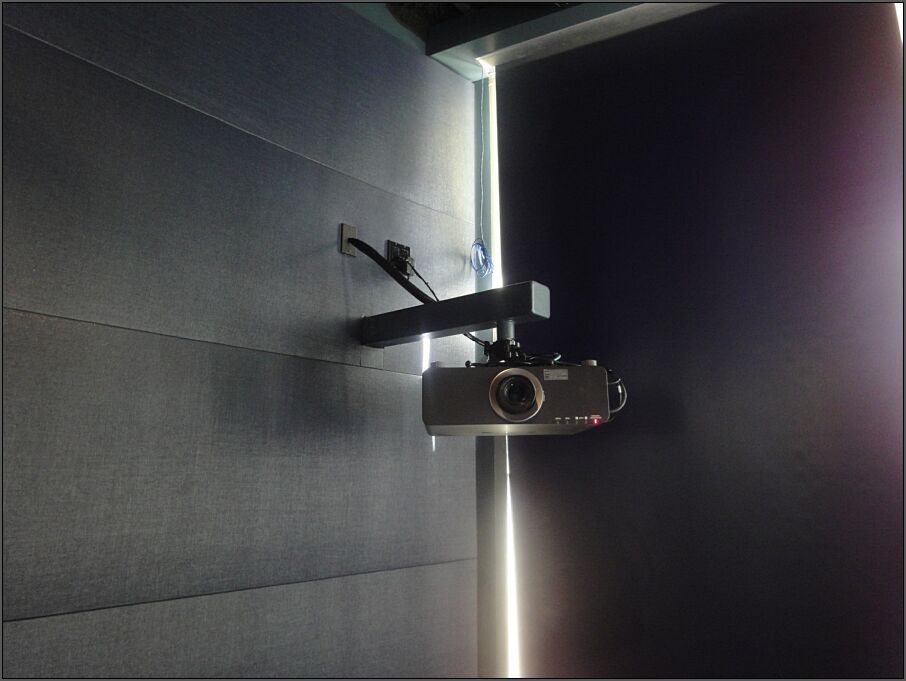 A square metal arm extends out from the wall with a short round rod extending down, to which a projector is mounted