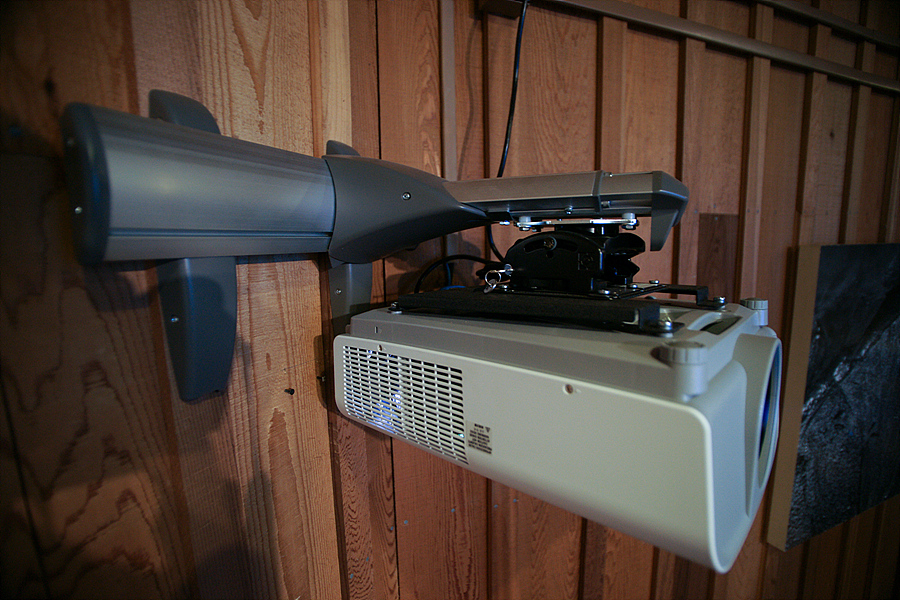 A short track is mounted to the wall. Attached to the track, extending out from the wall is another short track to which a projector is attached