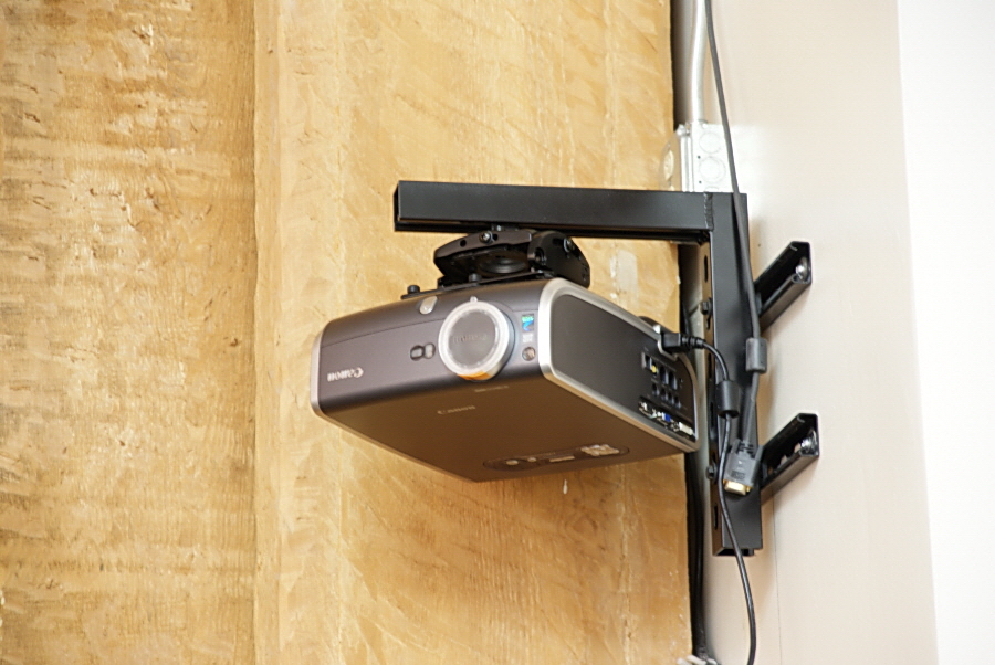 A projector is mounted to a short angle bracket that is attached to the wall by two rails