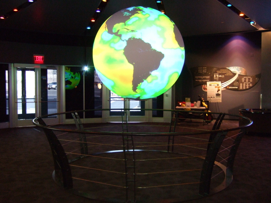 A circular metal rail flares up and out from the floor to keep visitors from touch Science On a Sphere at Clark Planetarium