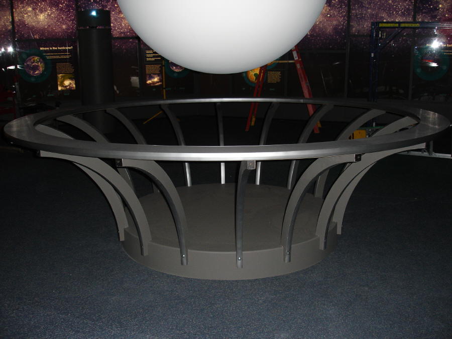 A flat metal hoop held up by posts that curve outward acts as a guard rail around Science On a Sphere at the Maryland Science Center