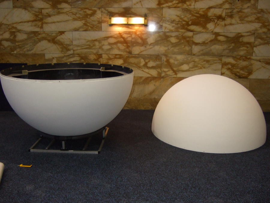 One half of a Science On a Sphere rests curved-side-down on a frame to keep it from rolling. The other half rests on the carpeted floor curved-side-up
