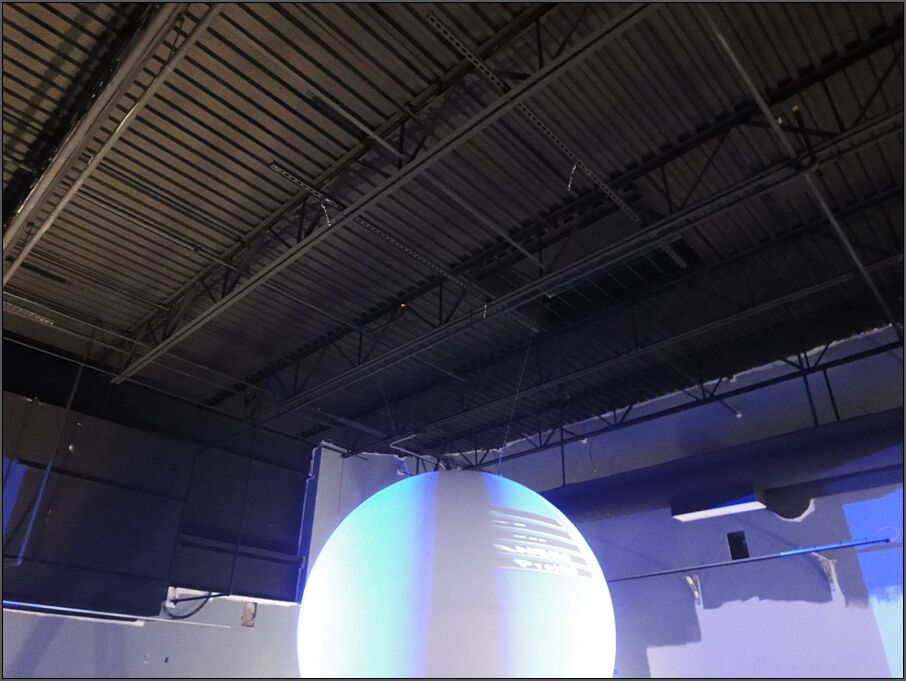 Science On a Sphere is suspended by three wires from two square metal brackets that run perpendicular to, and sit on top of the metal struts supporting the ceiling